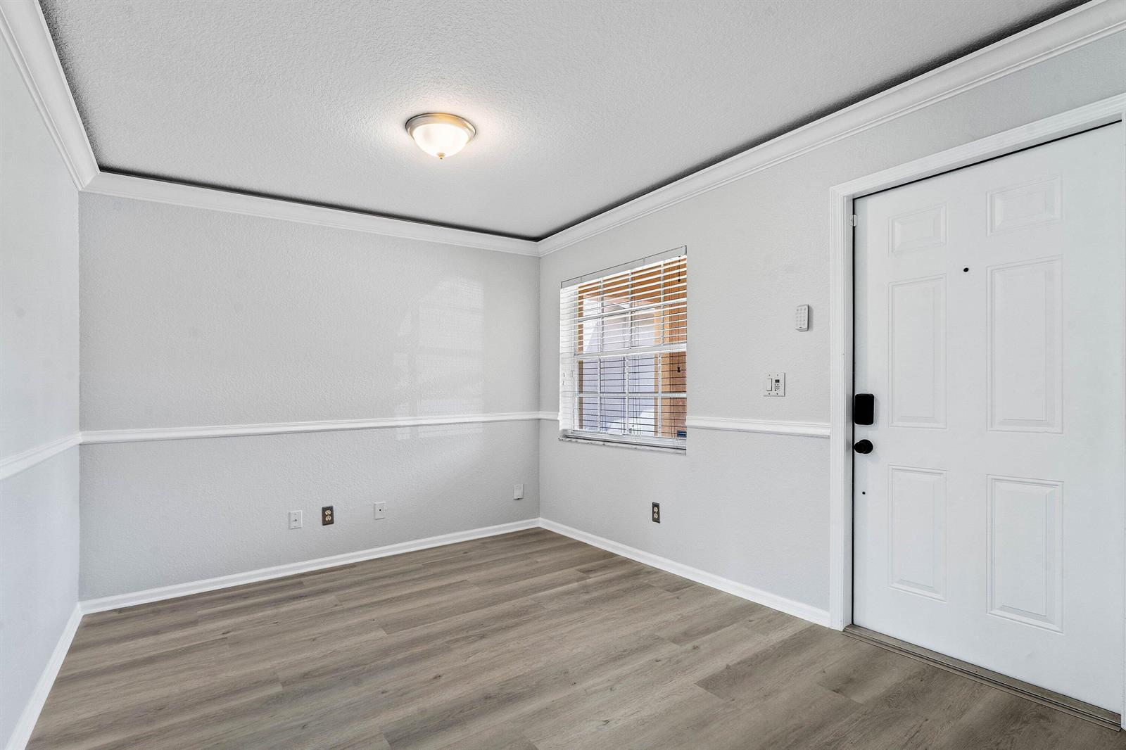 An empty room with light gray walls, white trim, wood-look flooring, and a front door — 3260 Commodore Court, West Palm Beach FL 33411, WEST PALM BEACH, FL