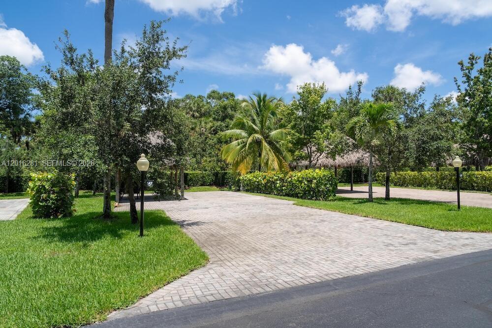 A paved driveway leads to a shaded tiki hut structure surrounded by lush tropical landscaping — 147 S Cortez Dr, Margate FL 33068, MARGATE, FL