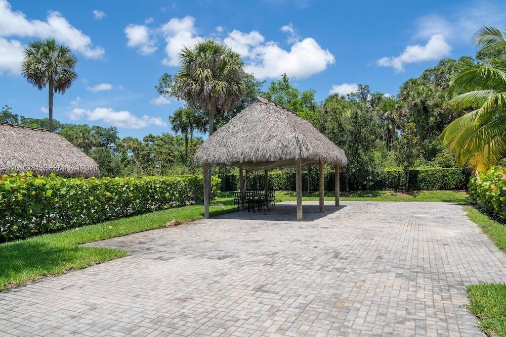A thatched-roof tiki hut stands on a paved patio surrounded by palm trees and hedges — 147 S Cortez Dr, Margate FL 33068, MARGATE, FL