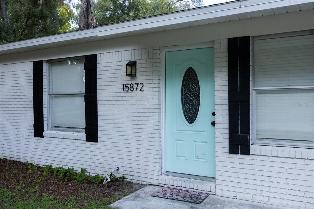 A white brick house exterior features a light blue front door and black window shutters — 15872 SW 133RD LANE, ARCHER, FL