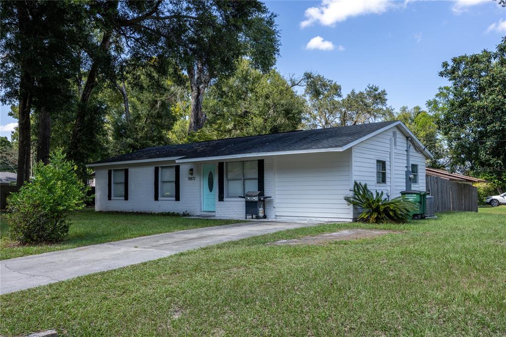 A single-story white house with a light blue front door and a concrete driveway — 15872 SW 133RD LANE, ARCHER, FL