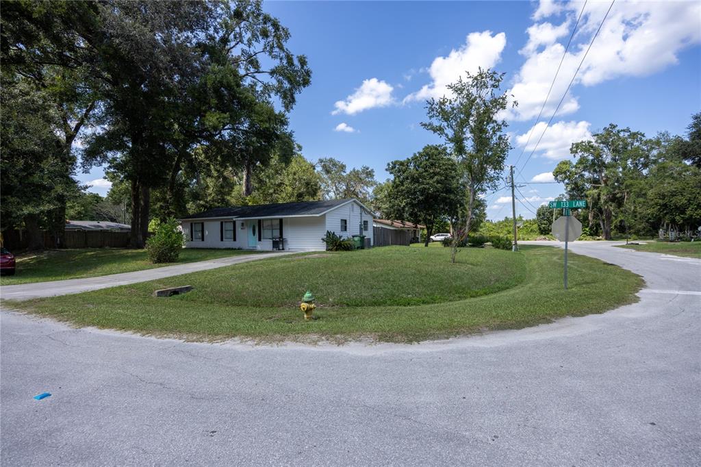 A single-story white house sits on a corner lot with a grassy yard and fire hydrant — 15872 SW 133RD LANE, ARCHER, FL