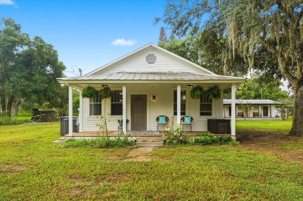 A white cottage with a metal roof and a front porch sits on a grassy lot — 4919 E COUNTY ROAD 542, LAKELAND, FL