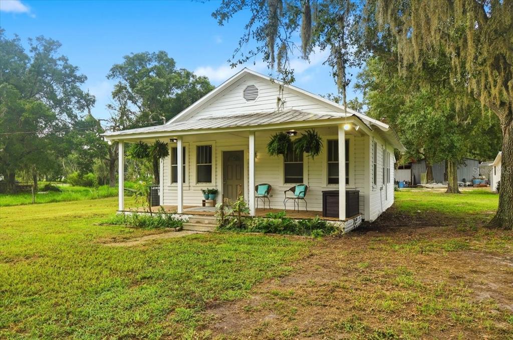 A white, single-story cottage with a front porch sits on a grassy lot with trees — 4919 E COUNTY ROAD 542, LAKELAND, FL
