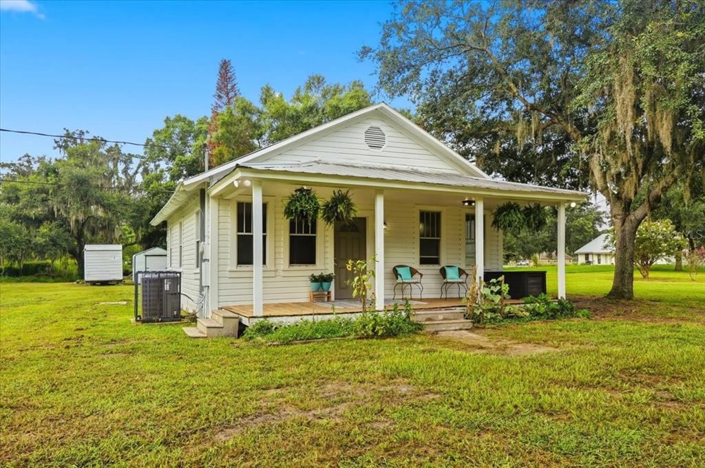 A white, single-story cottage with a front porch sits on a large, grassy lot — 4919 E COUNTY ROAD 542, LAKELAND, FL