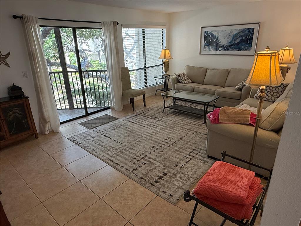 A living room features tile flooring, a large area rug, beige sofas, and a balcony — 6157 MIDNIGHT PASS ROAD UNIT F22, SARASOTA, FL