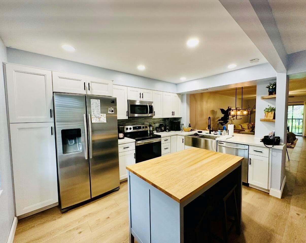 A kitchen features white cabinets, stainless steel appliances, a wood-topped island, and light wood flooring — 701 Avenue L Apt 204a, Delray Beach FL 33483, DELRAY BEACH, FL