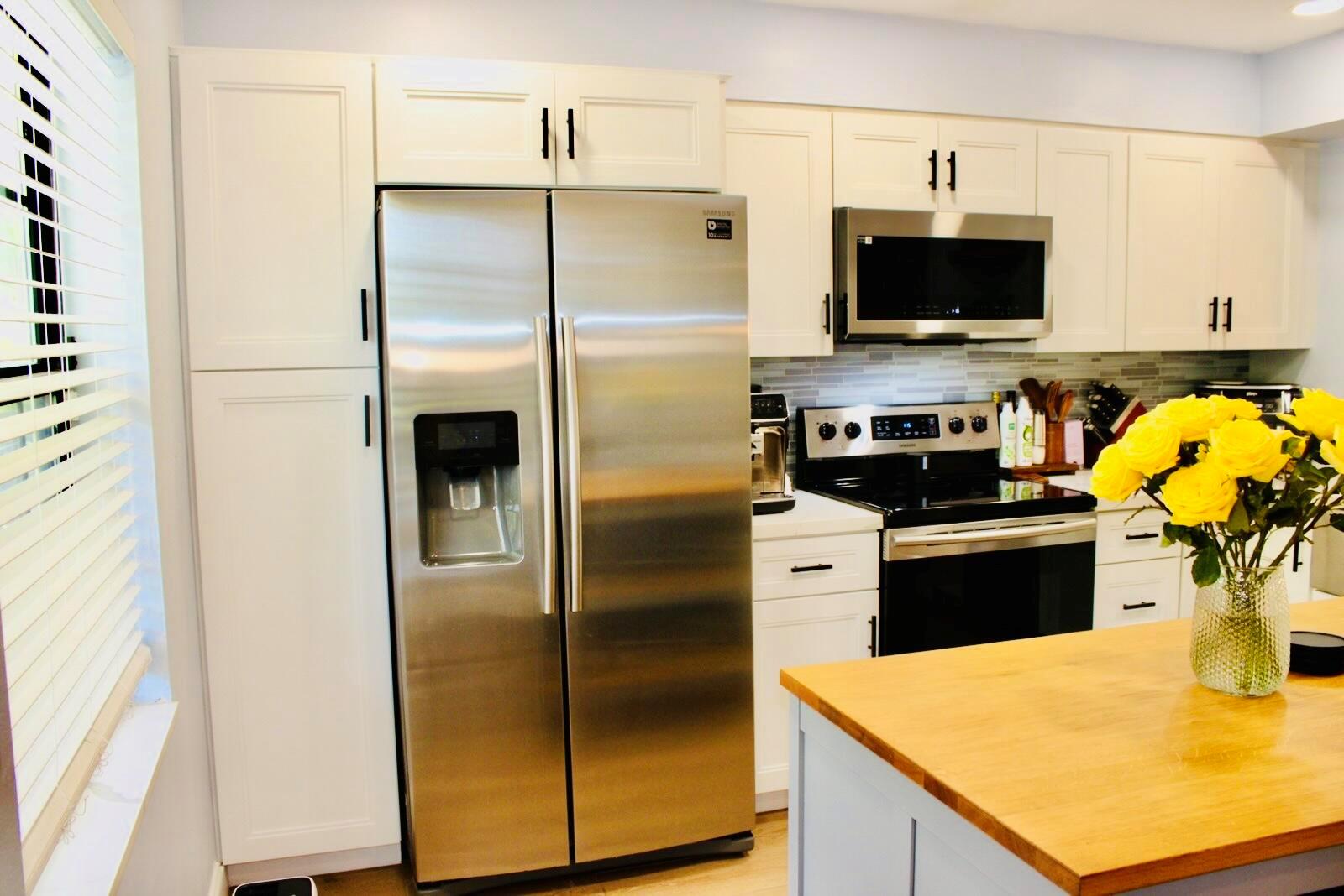 A kitchen features white cabinets, stainless steel appliances, and a wooden island with yellow flowers — 701 Avenue L Apt 204a, Delray Beach FL 33483, DELRAY BEACH, FL