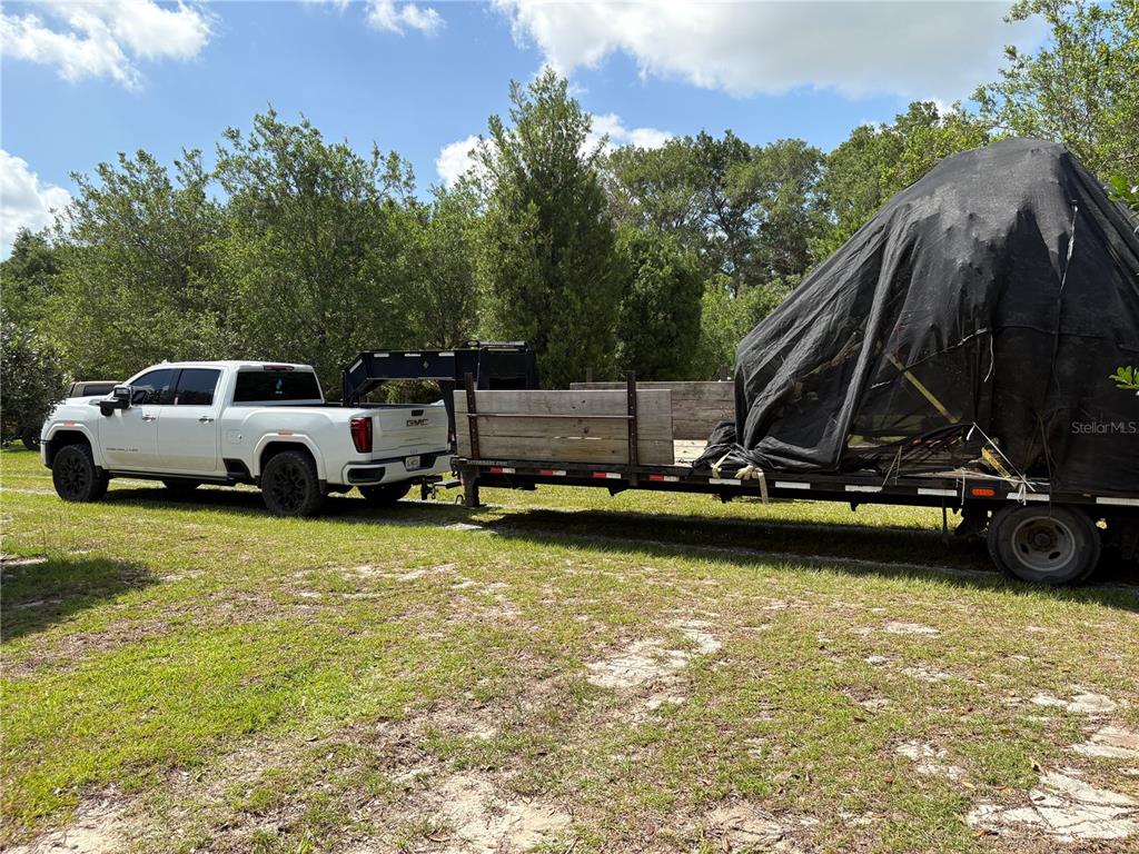 A white pickup truck is hitched to a flatbed trailer carrying a large covered object — 1238 S US 301, SUMTERVILLE, FL
