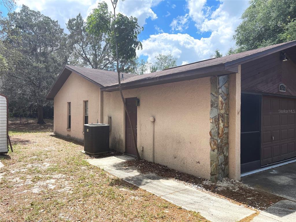 The exterior side of a tan stucco house features a door, an HVAC unit, and stone accents — 5526 CACTUS CIRCLE, SPRING HILL, FL