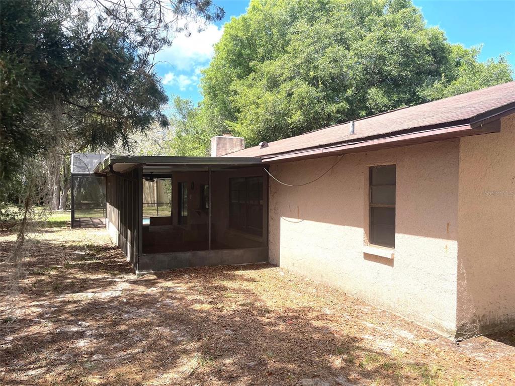 A beige house exterior features a large screened-in porch and a single window — 5526 CACTUS CIRCLE, SPRING HILL, FL