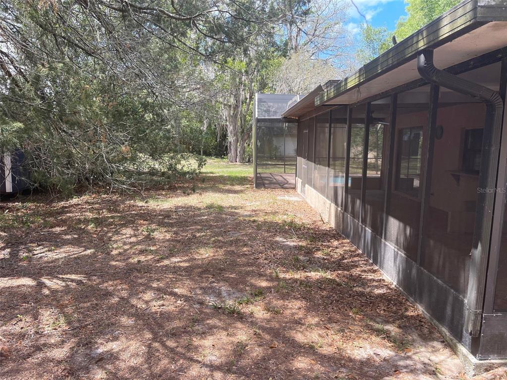 A screened-in porch runs along the side of a house next to a wooded yard — 5526 CACTUS CIRCLE, SPRING HILL, FL