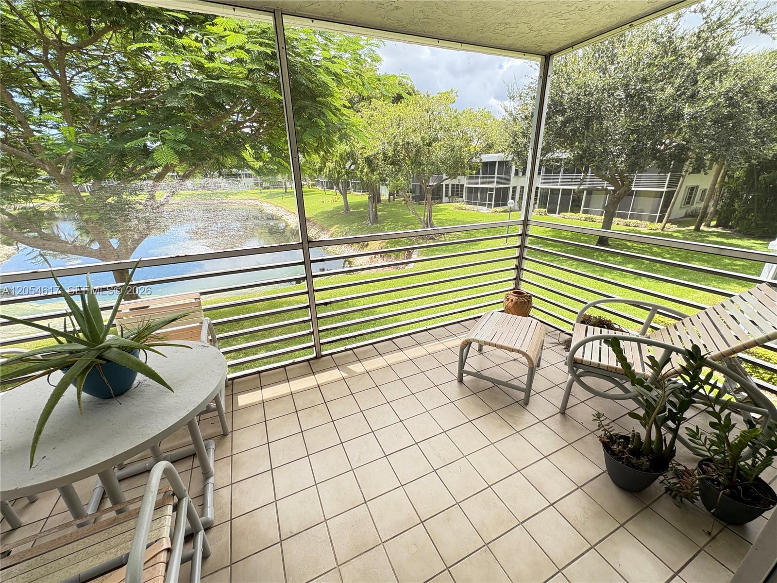 A screened-in balcony with tile flooring overlooks a pond and grassy lawn — 4280 Oaks Ter # 203, Pompano Beach FL 33069, POMPANO BEACH, FL