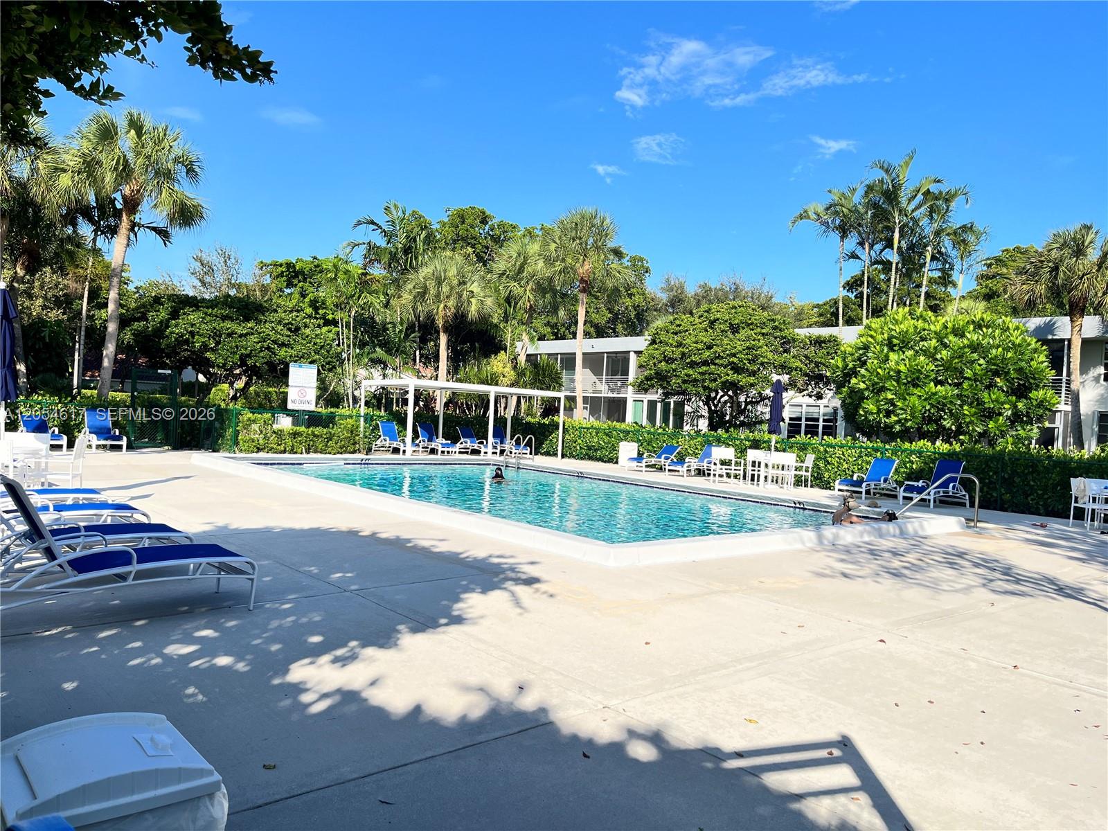 An outdoor swimming pool surrounded by lounge chairs, palm trees, and a residential building — 4280 Oaks Ter # 203, Pompano Beach FL 33069, POMPANO BEACH, FL