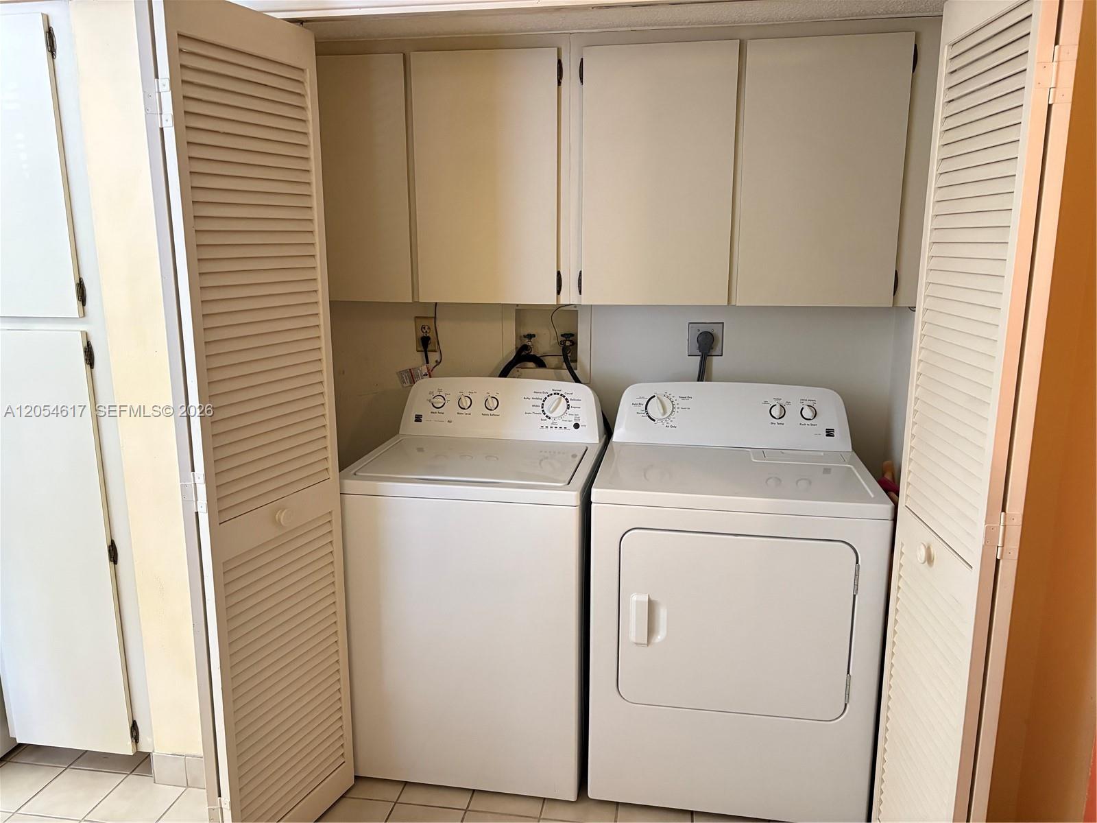 A laundry closet contains a white top-load washer and dryer beneath wall-mounted cabinets — 4280 Oaks Ter # 203, Pompano Beach FL 33069, POMPANO BEACH, FL