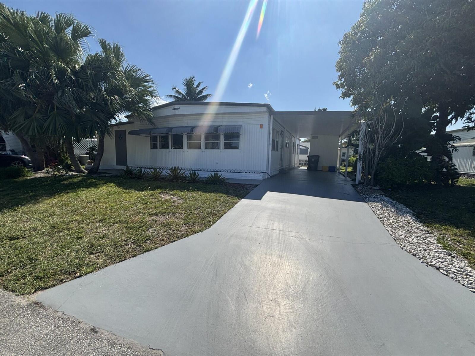 A white mobile home features a gray driveway, a carport, and surrounding palm trees — 6445 Cypress Lane, Atlantis FL 33462, ATLANTIS, FL