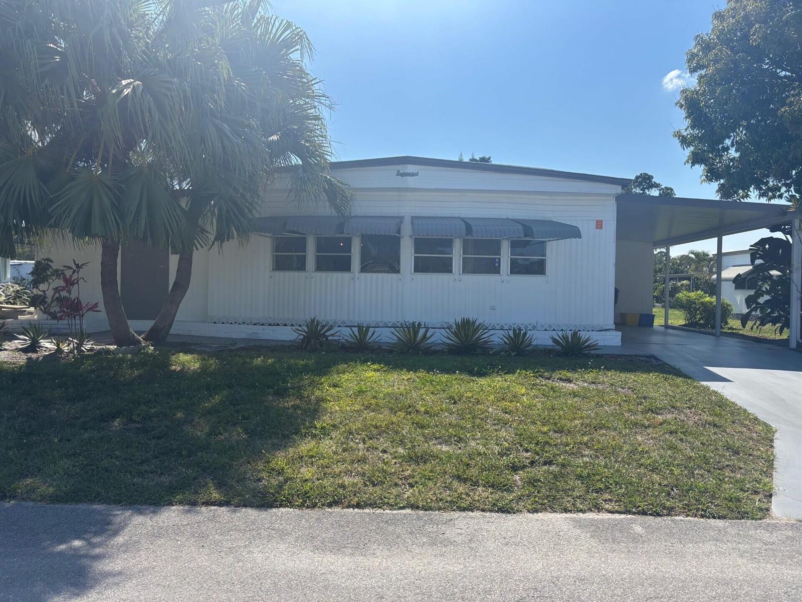 A white mobile home features a palm tree, a carport, and a grassy front yard — 6445 Cypress Lane, Atlantis FL 33462, ATLANTIS, FL