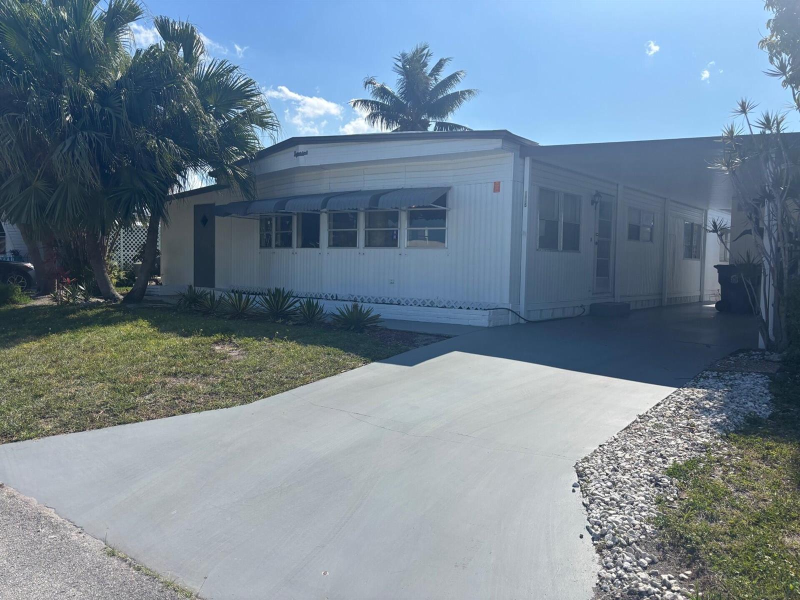 A white mobile home with a gray driveway and a carport under a blue sky — 6445 Cypress Lane, Atlantis FL 33462, ATLANTIS, FL