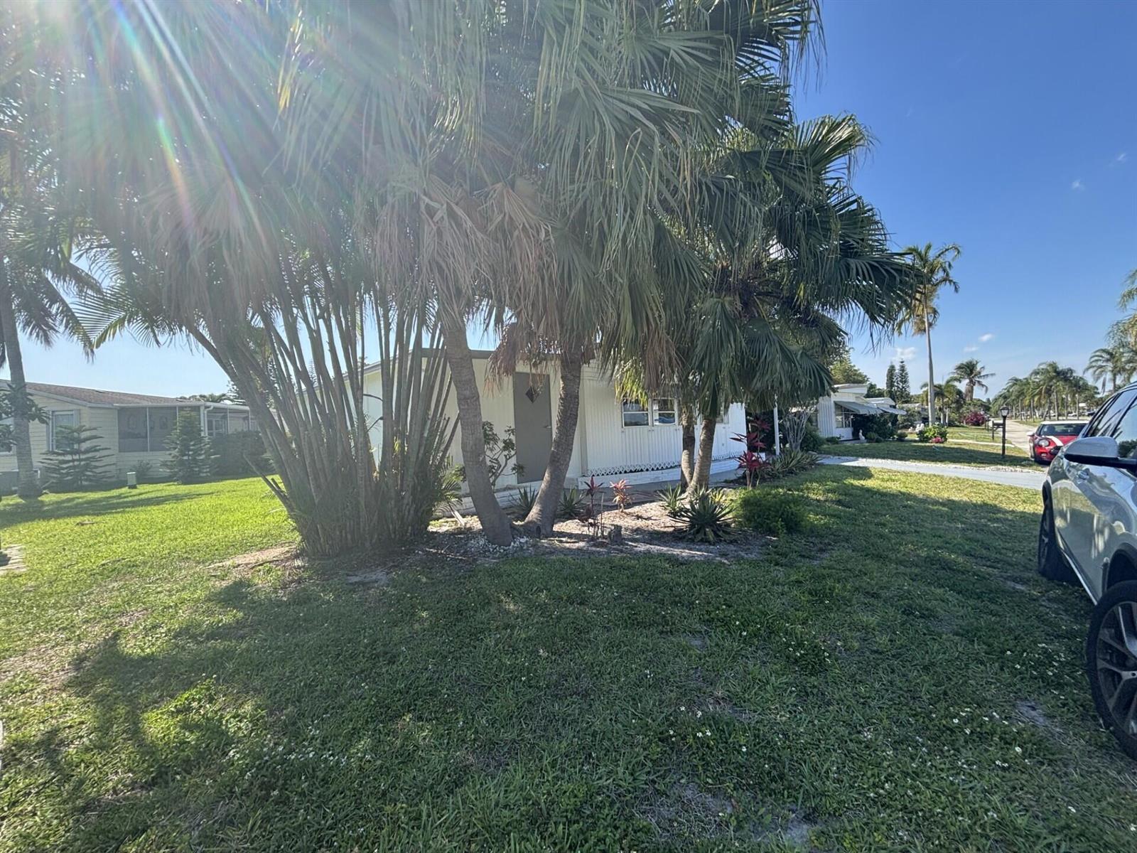 A white mobile home sits behind a cluster of palm trees on a grassy lot — 6445 Cypress Lane, Atlantis FL 33462, ATLANTIS, FL