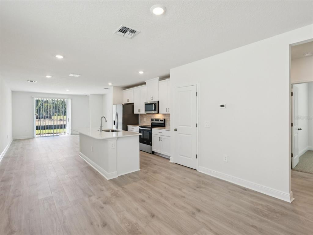 A bright, open-concept kitchen features white cabinetry, a central island, and light wood-look flooring — 887 SUNSHOWER DRIVE, LADY LAKE, FL
