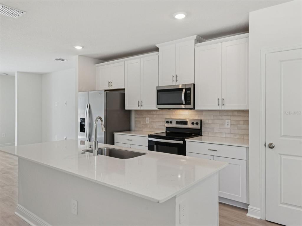 A modern kitchen features white cabinets, stainless steel appliances, and a large quartz-topped island — 887 SUNSHOWER DRIVE, LADY LAKE, FL