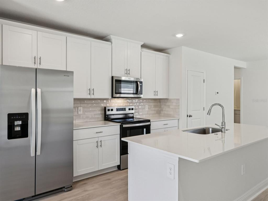 A modern kitchen features white cabinets, stainless steel appliances, and a white quartz island countertop — 887 SUNSHOWER DRIVE, LADY LAKE, FL