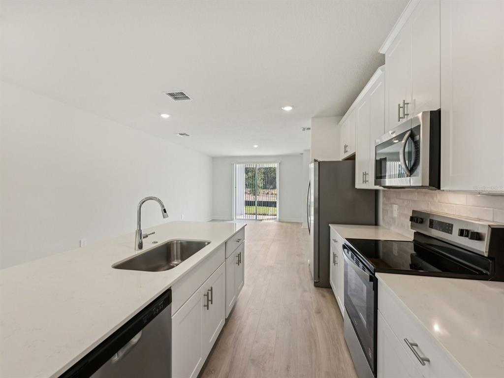 A modern kitchen features white cabinets, quartz countertops, stainless steel appliances, and light wood flooring — 887 SUNSHOWER DRIVE, LADY LAKE, FL