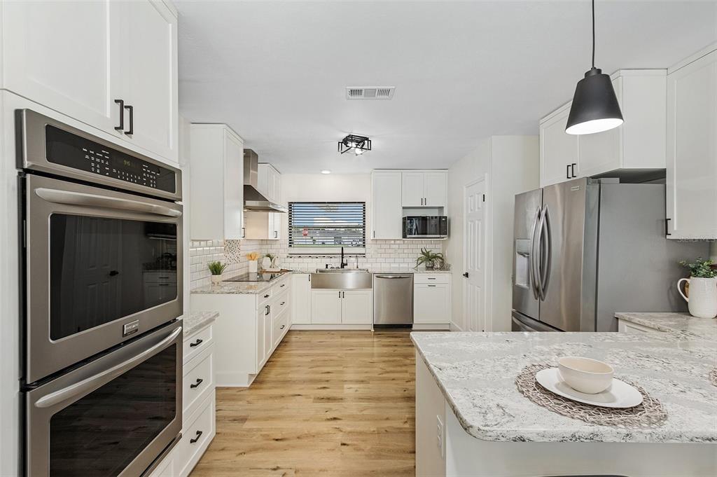 A modern kitchen features white cabinets, stainless steel appliances, granite countertops, and wood-look flooring — 191 CASA LANE, PUNTA GORDA, FL