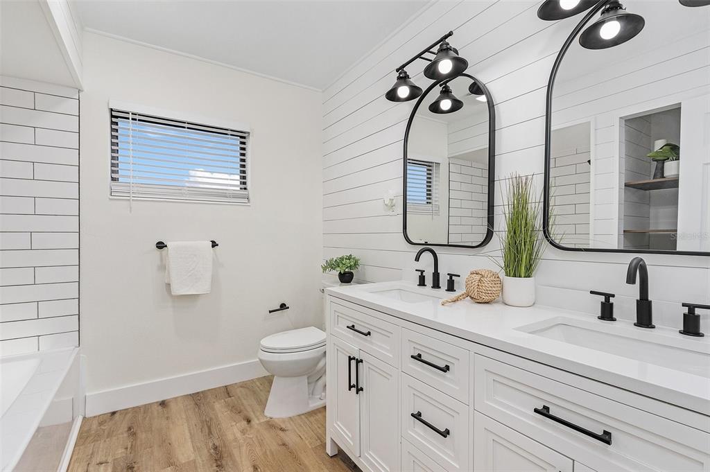 A modern bathroom features a double vanity, shiplap wall, arched mirrors, and wood-look flooring — 191 CASA LANE, PUNTA GORDA, FL