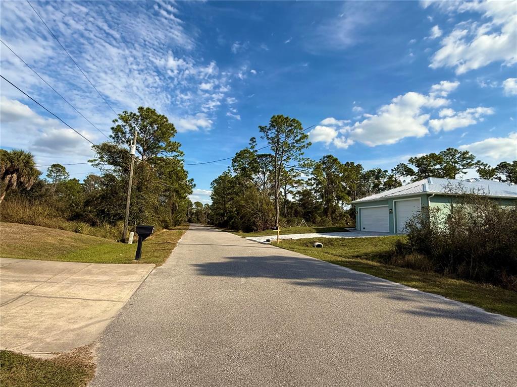 A paved road leads past a light green detached garage and surrounding trees under a sky — BURWIN AVENUE, NORTH PORT, FL
