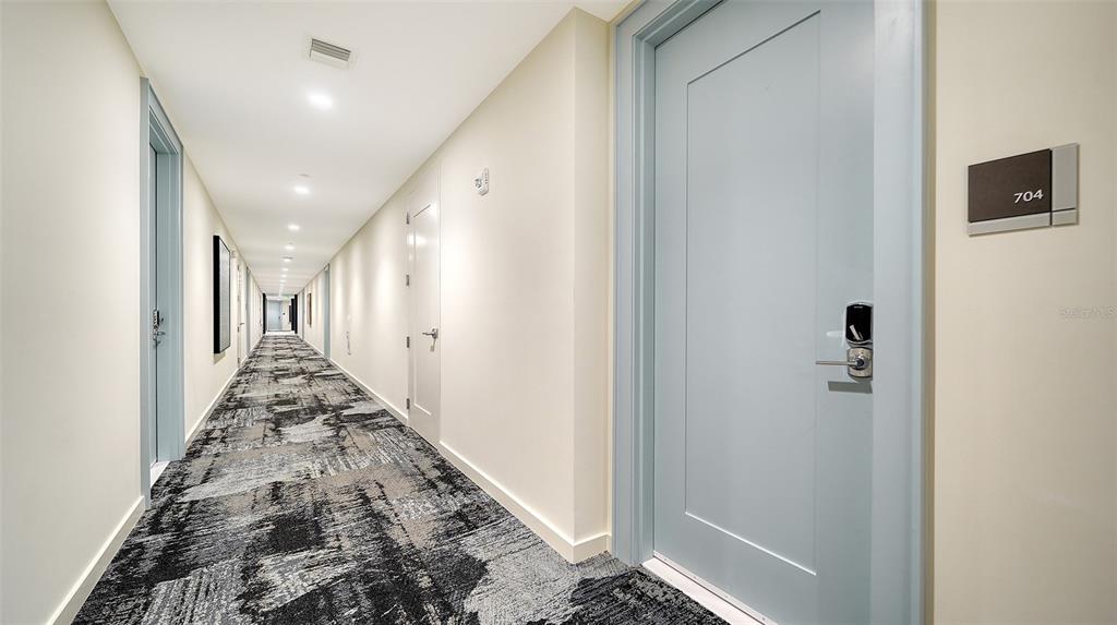 A long apartment hallway features patterned gray carpeting and light blue doors — 301 QUAY COMMONS DRIVE UNIT 704, SARASOTA, FL
