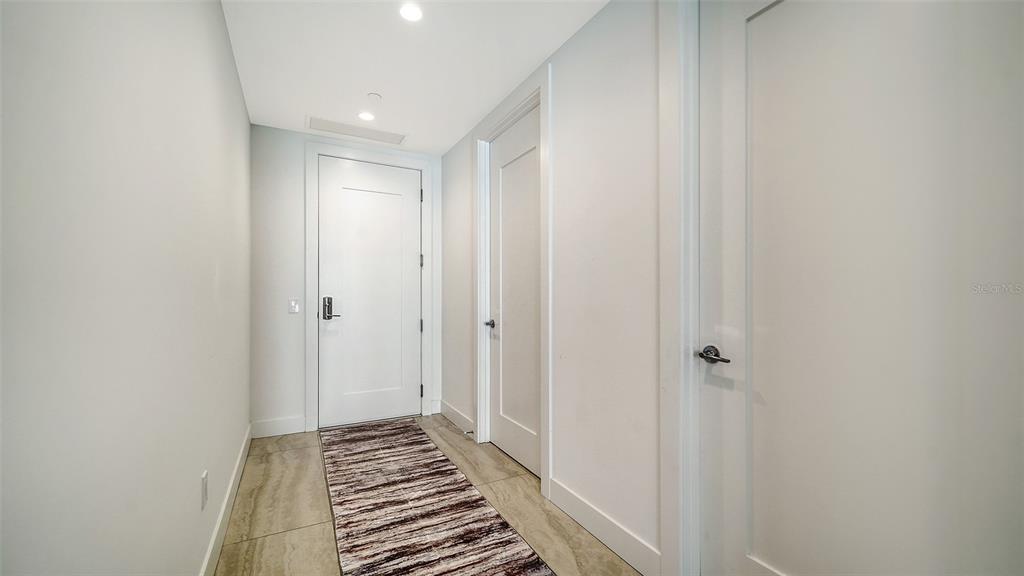 A hallway with light tile flooring, a patterned runner rug, and three white interior doors — 301 QUAY COMMONS DRIVE UNIT 704, SARASOTA, FL