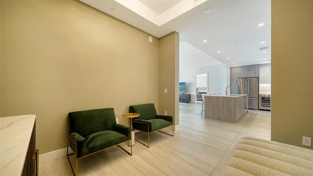 A room with two green velvet chairs leads into an open-concept kitchen with light flooring — 301 QUAY COMMONS DRIVE UNIT 704, SARASOTA, FL