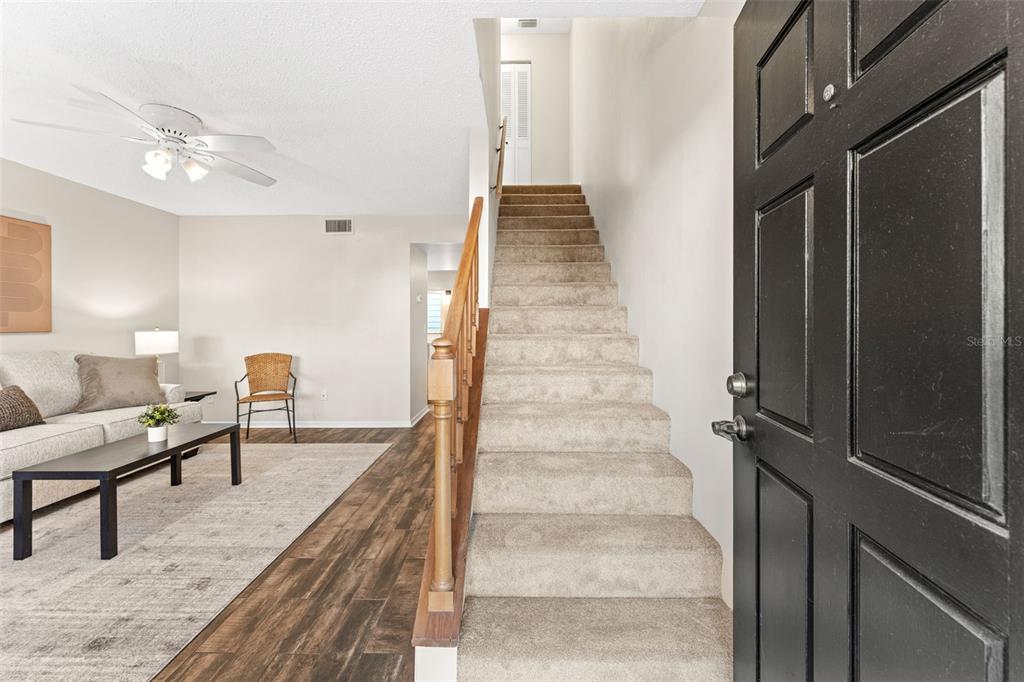 An entryway features a carpeted staircase, a black front door, and a living room area — 101 N PINE STREET UNIT 2, NEW SMYRNA BEACH, FL