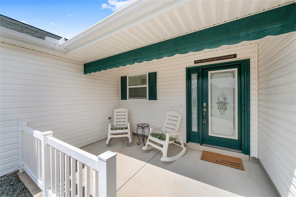 A covered front porch features white siding, two rocking chairs, and a green door — 17602 SE 82ND WOODLAWN AVENUE, THE VILLAGES, FL