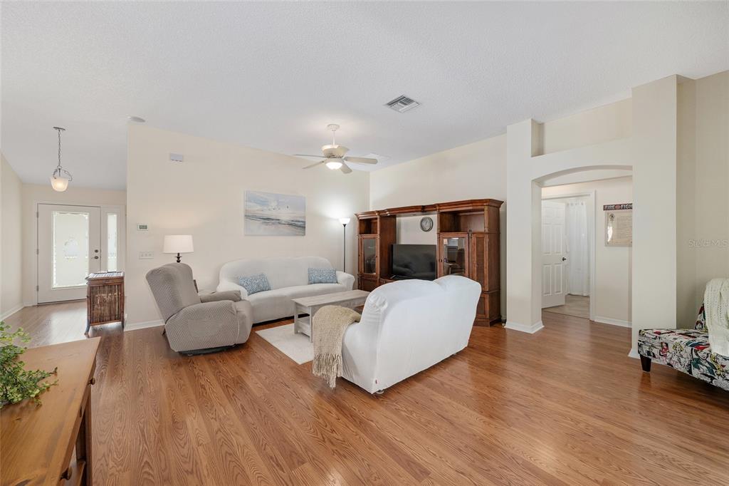 A living room features hardwood floors, a white sofa, a recliner, and a wooden entertainment center — 17602 SE 82ND WOODLAWN AVENUE, THE VILLAGES, FL
