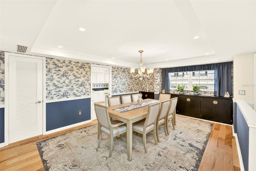 A dining room features a wooden table, six chairs, patterned wallpaper, and a dark sideboard — 131 BLUFF VIEW DRIVE UNIT 401, BELLEAIR BLUFFS, FL