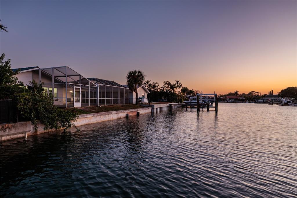 A waterfront house with a screened-in pool enclosure at sunset along a canal — 1985 MICHIGAN AVENUE NE, ST PETERSBURG, FL