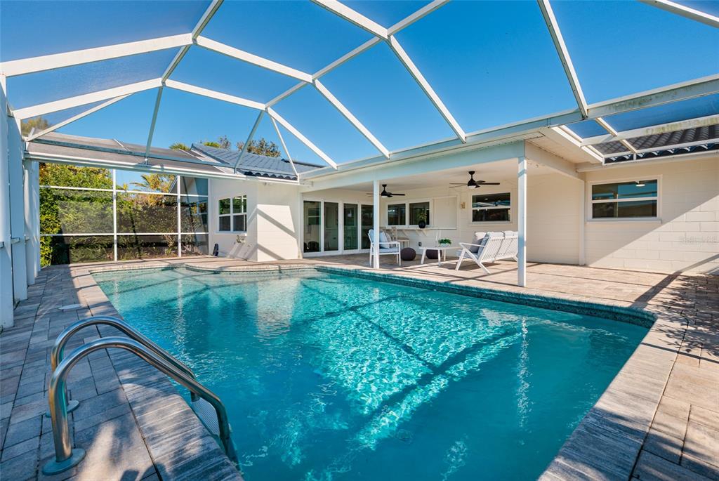 A swimming pool with a metal ladder sits inside a screened-in patio area — 1985 MICHIGAN AVENUE NE, ST PETERSBURG, FL