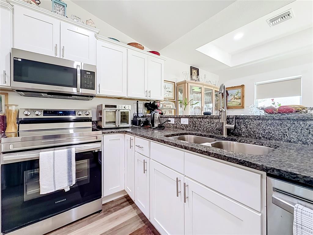 A kitchen features white cabinets, stainless steel appliances, and dark granite countertops — 628 MARION OAKS TRAIL, OCALA, FL