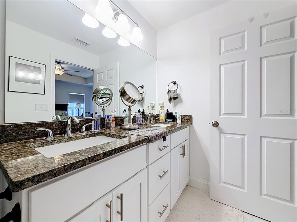 A bathroom vanity features a granite countertop, white cabinets, and a large wall mirror — 628 MARION OAKS TRAIL, OCALA, FL