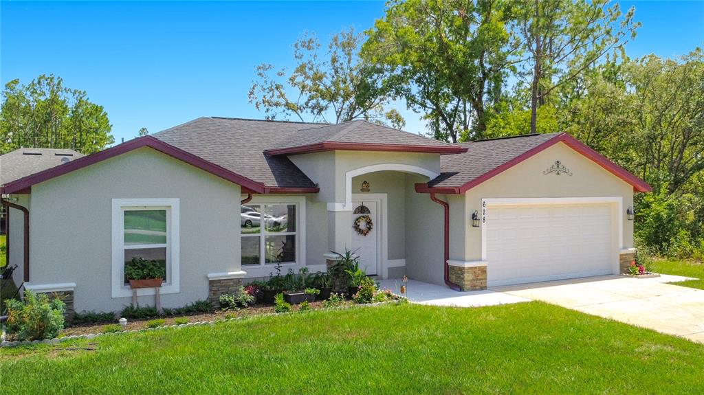A single-story house with a light-colored stucco exterior, red trim, and a two-car garage — 628 MARION OAKS TRAIL, OCALA, FL