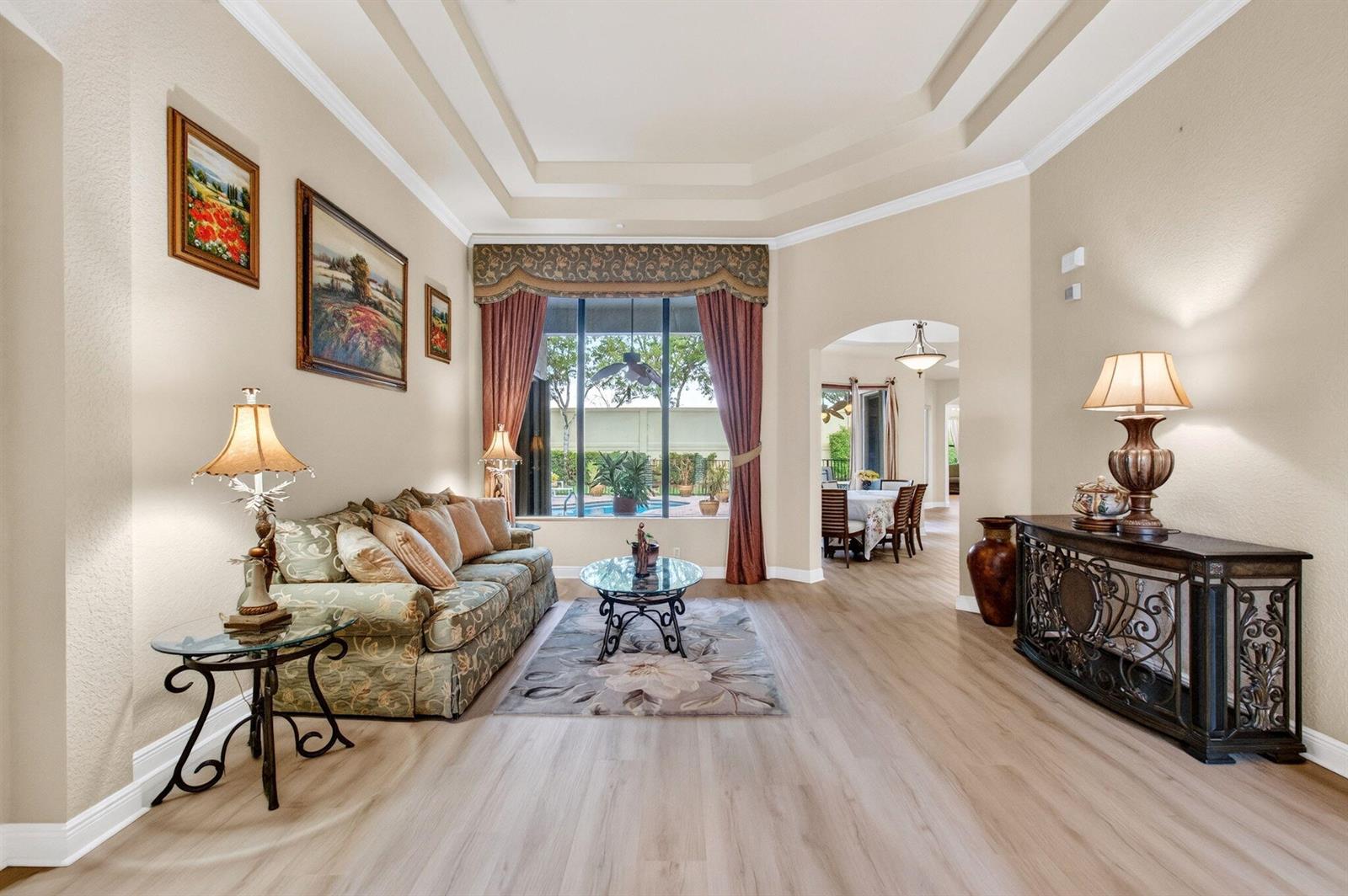 A living room with light wood floors, a patterned sofa, and a view of a pool — 16211 Rosecroft Terrace, Delray Beach FL 33446, DELRAY BEACH, FL