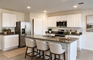 A modern kitchen features white cabinets, a granite island with three stools, and stainless appliances — 2017 MAPLE RIDGE DRIVE, ZELLWOOD, FL