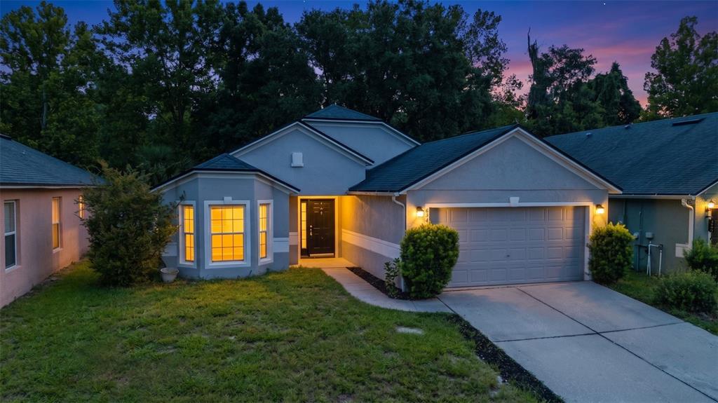 A single-story house with a gray stucco exterior, a two-car garage, and a bay window — 634 SPRING CAVERN AVENUE, ORANGE CITY, FL