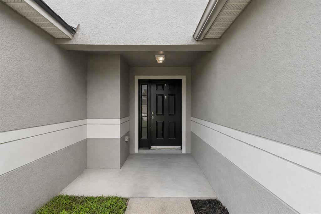 A front entryway features a black door with a side window and gray stucco walls — 634 SPRING CAVERN AVENUE, ORANGE CITY, FL