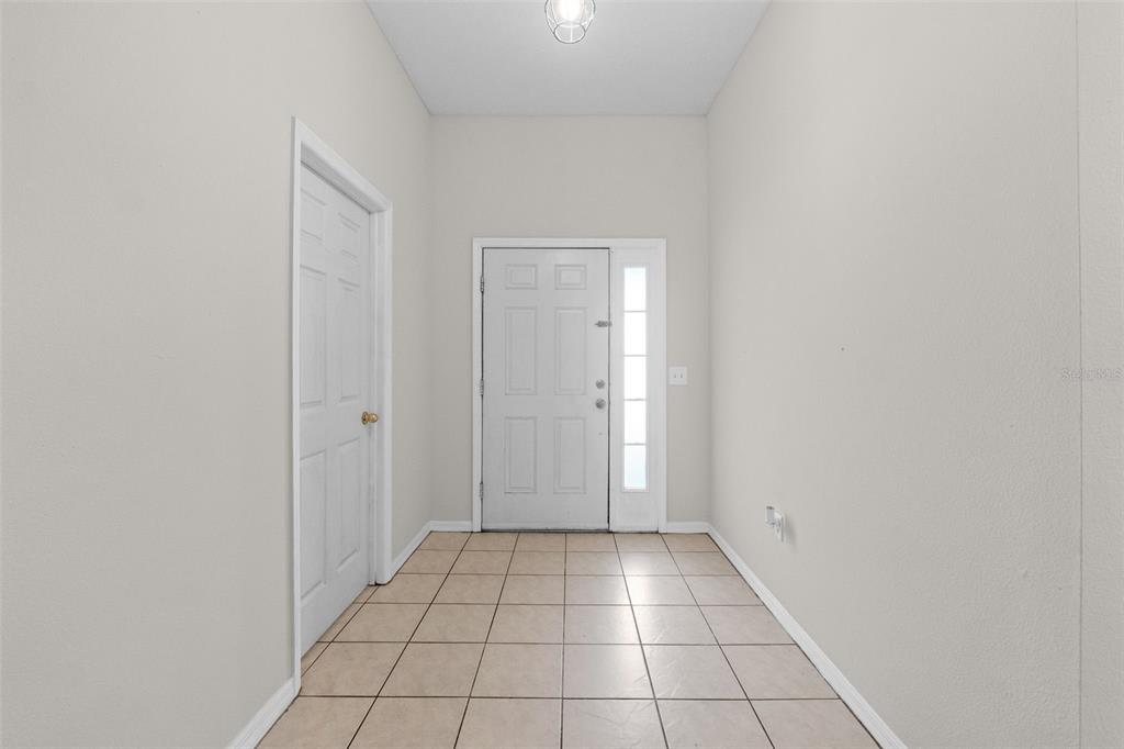 An entryway features light-colored tile flooring, white walls, a front door with sidelights, and a closet — 634 SPRING CAVERN AVENUE, ORANGE CITY, FL