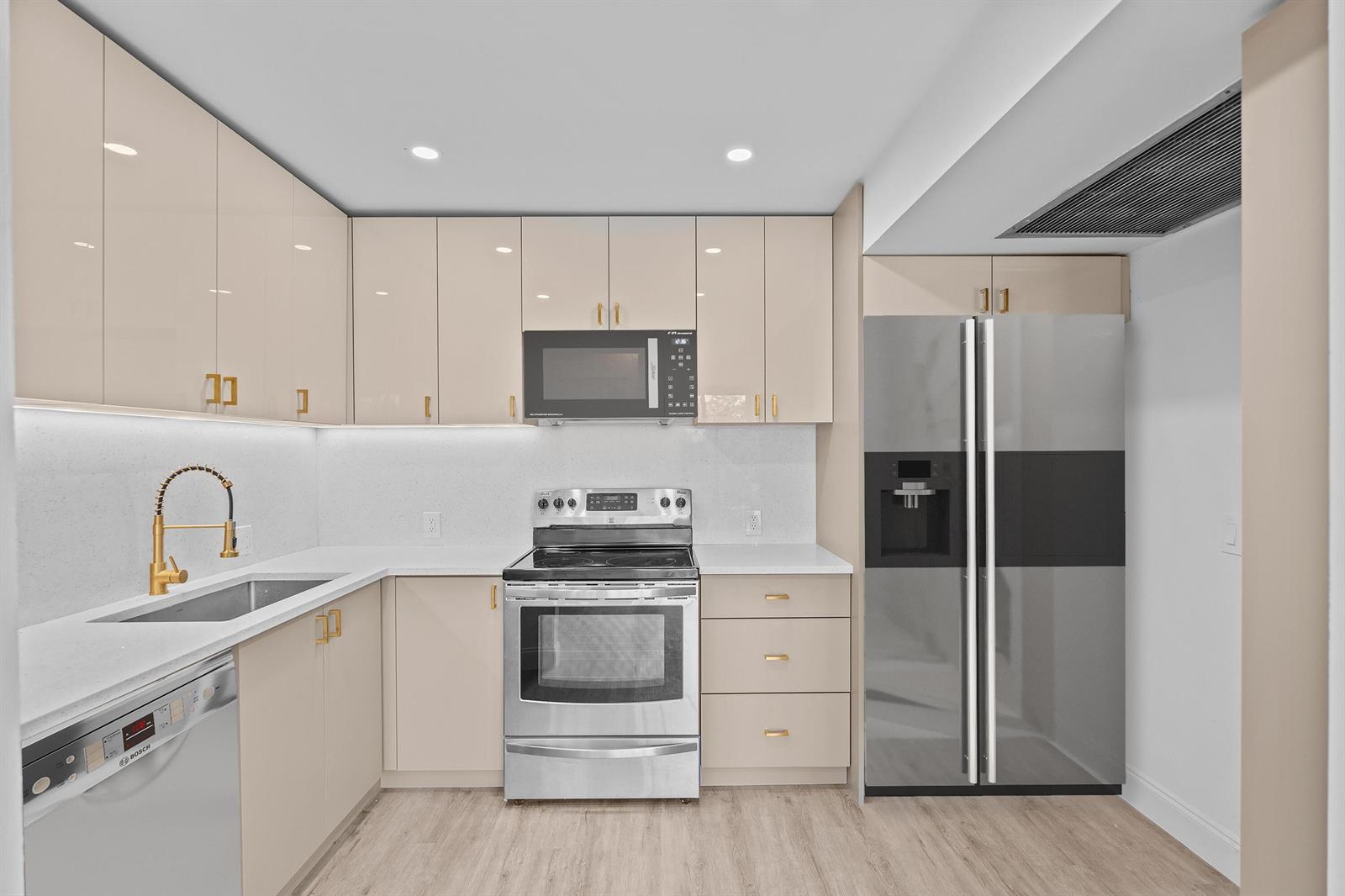 A modern kitchen features light beige cabinets, stainless steel appliances, and a white quartz countertop — 204 Mansfield E # 204, Boca Raton FL 33434, BOCA RATON, FL