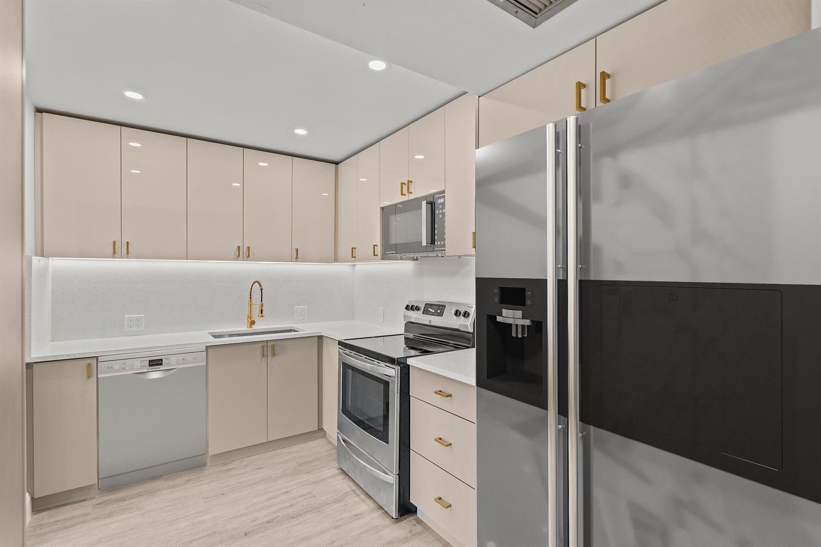 A modern kitchen features light-colored cabinetry, stainless steel appliances, and gold hardware — 204 Mansfield E # 204, Boca Raton FL 33434, BOCA RATON, FL