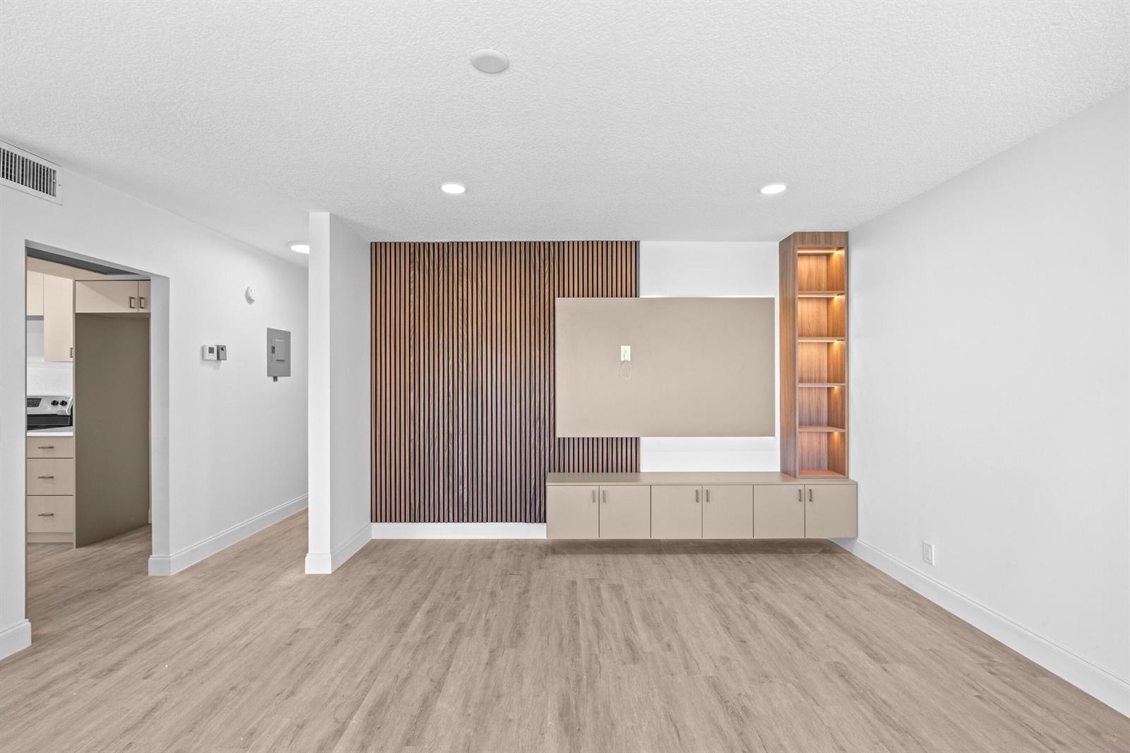 A living room features light wood flooring, a slatted wood accent wall, and built-in cabinetry — 204 Mansfield E # 204, Boca Raton FL 33434, BOCA RATON, FL